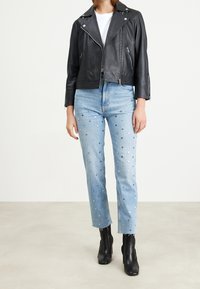 Svart lädermotorcykeljacka över en vit T-shirt, parat med ljusblå jeans med silverfärgade prickdetaljer och svarta anklarstövlar.