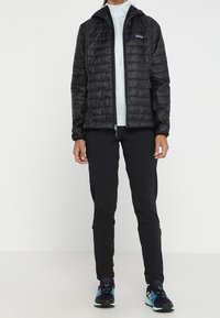 Svart vadderad jacka med huva, lätt material, dragkedjestängning. Kombinerad med svarta byxor och sportskor med blå accenter.