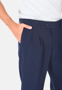 Pantaloni a pieghe blu navy realizzati in tessuto liscio, dotati di chiusura con bottone e tasche laterali, con una vita aderente e un design a gamba dritta.