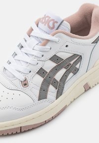 Vita lädersneaker med rosa och grå accenter, med en texturerad sula, perforeringar och en vadderad krage för komfort.