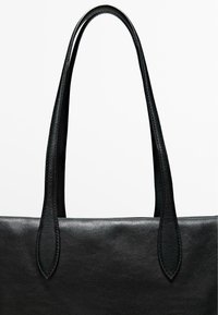 Borsa tote in pelle nera con due manici allungati. Texture liscia, design minimalista e linee pulite senza hardware o accenti aggiuntivi.