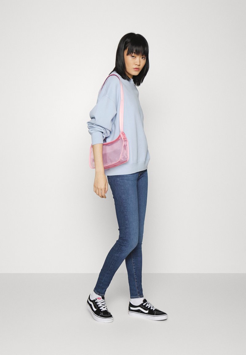 Jasnoniebieski oversize'owy sweter, średnio niebieskie rurki, czarno-białe sneakersy oraz różowa przezroczysta torba na ramię.