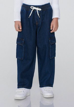 Blaue Denim-Cargohosen mit elastischem Bund, Kordelzug, zwei Seitentaschen und zwei Cargotaschen. Kombiniert mit weißen Sneakern.
