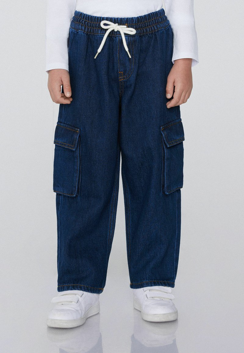Modré džínové cargo kalhoty s elastickým pasem, šnůrkou, dvěma bočními kapsami a dvěma cargo kapsami. Spárovány s bílými teniskami.