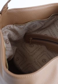 Beige läderhandväska med en slät textur inuti, utrustad med en dragkedjeficka och ett tygfoder med präglat "Café Noir"-mönster.