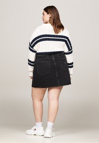 Pull blanc avec des rayures marine, jupe en denim noire, baskets blanches et chaussettes montantes. Présente une texture côtelée et des poches classiques en denim.