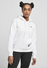 Hvit hettegenser med frontlomme, snøring til hetten og en liten logo på brystet. Myk stoff og ribbestrikkede mansjetter. Kombinert med svarte leggings.