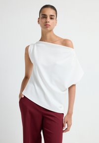 Top bianco beh, con spalle scoperte e un design drappeggiato, realizzato in tessuto leggero; abbinato a pantaloni tailored bordeaux; texture liscia.