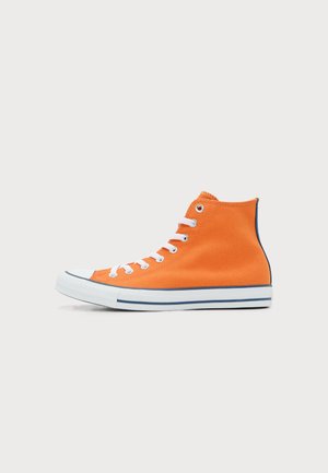 Zapatilla de lona de caña alta en naranja brillante con suela de goma blanca, cordones blancos y ojales metálicos, vista desde un lado sobre un fondo claro.