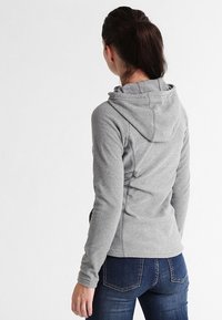 Šedá mikina na zip s kapucí, dlouhými rukávy a texturovanou tkaninou. Obsahuje švy a nastavitelnou šňůrku na kapuci.