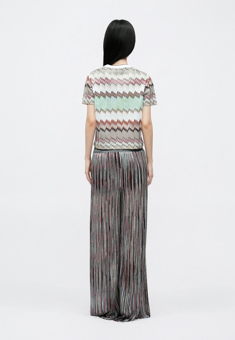 Top multicolor con patrón de zigzag, confeccionado en tela ligera, combinado con pantalones anchos, plisados y brillantes en tonos oscuros.