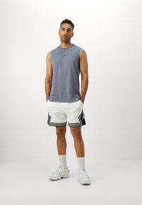 Top grigio senza maniche con logo nero, abbinato a pantaloni corti in rete bianchi con accenti neri e un motivo geometrico. Sneakers bianche e calzini.