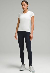 Weißes Sporthemd mit kurzen Ärmeln und navyfarbene elastische Leggings, kombiniert mit grauen Sneakers mit hellen Akzenten. Glatte Stoffoberfläche.