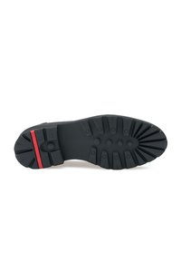 Zwarte rubberen zool met diepe loopvlakken voor grip. Heeft een rode accentlijn en cirkelvormige dempingpunten voor comfort.