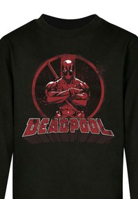 Mustern black sweatshirt, mille punase graafikaga maskeeritud tegelasega, kellel on käed rinnal ja katana. All on "DEADPOOL" tekst julges punases fondis.