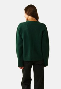 Grön kortärmad tröja med ribbat fåll och muddar. Har en kontrasterande beige krage. Mjuk textur, oversized passform och avslappnad stil.