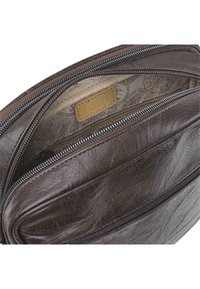 Interior de un bolso de cuero marrón con un forro estampado, que cuenta con un compartimento principal y un bolsillo con cremallera. Incluye un parche con el logo.