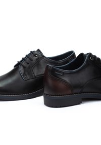 Chaussures en cuir noir et marron avec une finition lisse, bout rond, à lacets, avec des coutures contrastées et une semelle en caoutchouc.