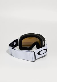 Lunettes de protection avec une sangle blanche, des bords noirs et des verres teintés marron. Elles sont dotées d'un rembourrage doux et d'une boucle réglable pour un maintien sécurisé.