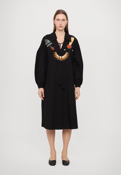 Black dress with a collar, puffed sleeves, and colorful embroidery featuring a flower, sun, and geometric shapes. Tasseled drawstring detail.