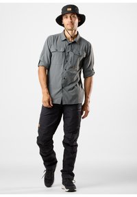 Szary longsleeve z dwoma przednimi kieszeniami, zestawiony z czarnymi spodniami cargo. Czarne kapelusz typu bucket i czarne buty sportowe dopełniają outfitu.