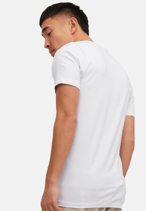 Mann trägt ein schlichtes weißes T-Shirt mit kurzen Ärmeln und blickt über seine linke Schulter nach unten, wobei die Rückseite und die linke Seite des Shirts gezeigt werden.