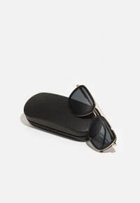 Ochelari de soare cu lentile negre, detalii din metal aurit și rame Square, așezați pe un toc negru din material dur, gravat cu "BOSS."