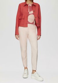 Korallfärgad kavaj med två stora framfickor, lager på lager över en mönstrad topp och tillsammans med ljusrosa skräddarsydda byxor och vita sneakers.