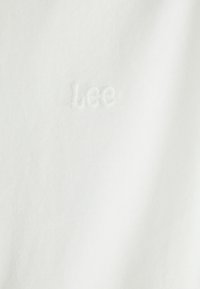 Tissu blanc à texture douce avec un logo "Lee" brodé en fil ton sur ton pour un détail de marque subtil.
