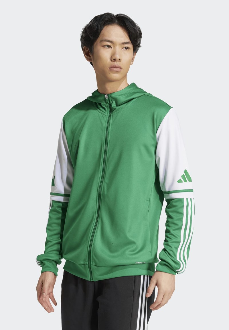 Giacca sportiva verde con accenti bianchi, zip frontale, cappuccio e tre strisce sulle maniche. Realizzata in tessuto liscio e leggero.