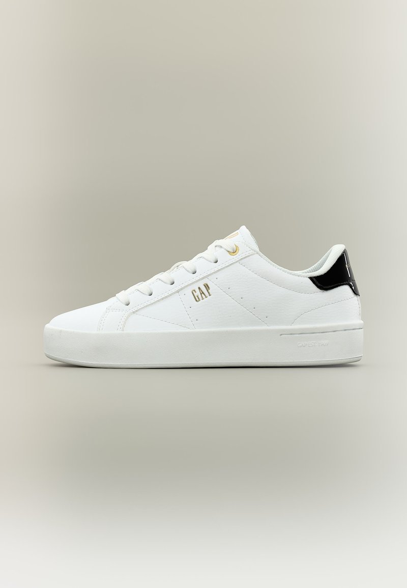 Baskets blanches basses à lacets, logo "GAP" doré sur le côté et languette de talon noire, présentées sur un fond neutre.