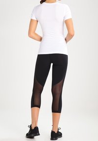 Camiseta blanca de manga corta ajustada combinada con leggings capri negros con paneles de malla, textura suave y cinturilla elástica, adecuados para ropa activa.