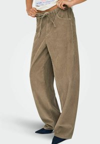 Platākas, khaki krāsas kordūras bikses ar teksturētu virsmu, ar aukliņu jostasvietā un sānu kabatām. Kombinētas ar tumši ziliem norādītiem apaviem.