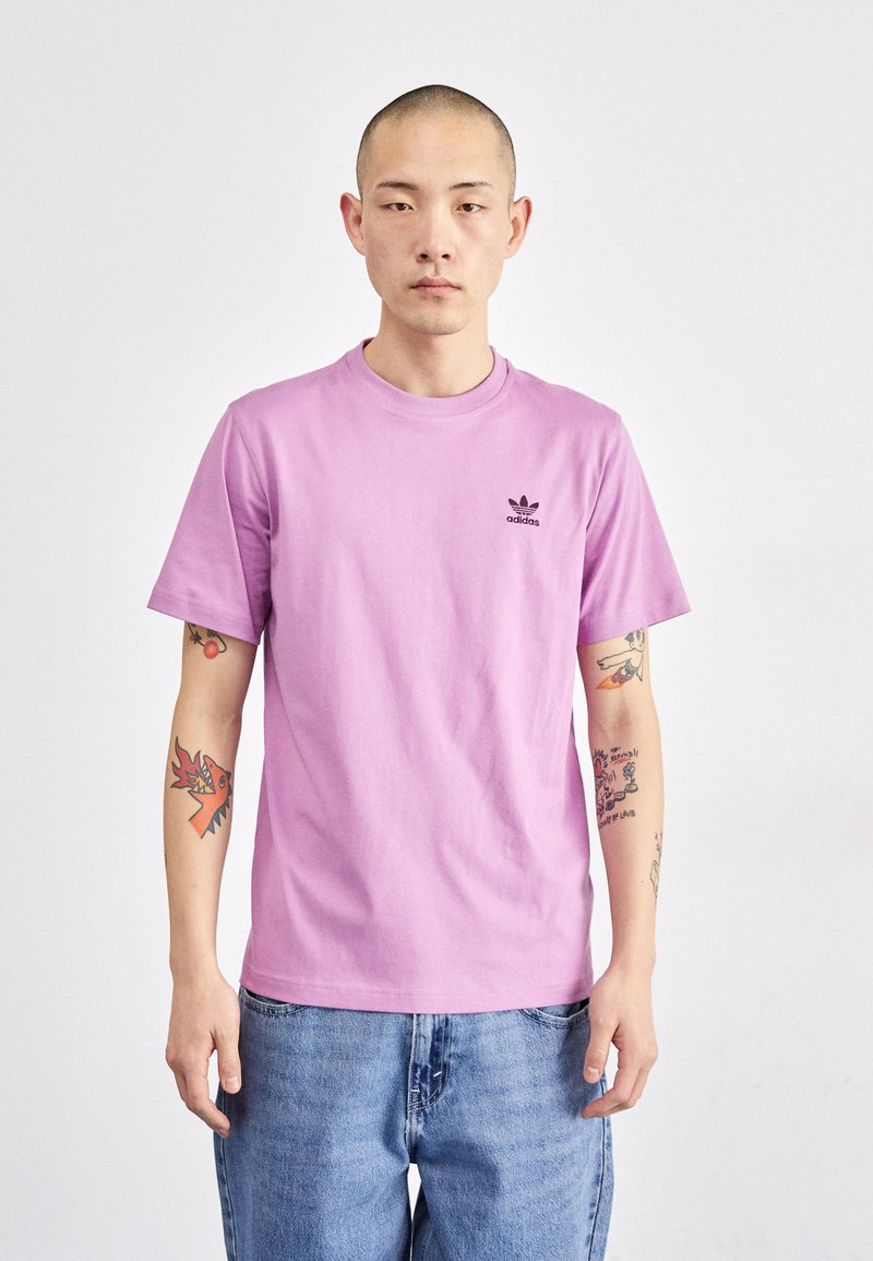 Világoslila pamut póló rövid ujjal és kerek nyakkivágással; az elején, a bal mellen egy kis fekete Adidas logó található. Kék farmernadrággal viselve.