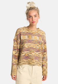 Sweter robiony na drutach o luźnym kroju, z wielokolorowym wzorem w odcieniach żółtego, fioletowego i niebieskiego; ściągacze przy mankietach i u dołu.