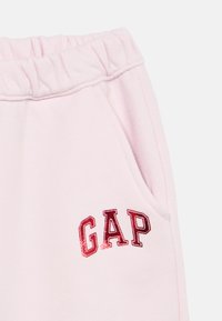 Ροζ ανοιχτό παντελόνι φόρμας με ελαστική μέση, που διαθέτει πλαϊνή τσέπη και κόκκινη λαμπερή κεντημένη στάμπα με το λογότυπο "GAP" στο μπροστινό μέρος.