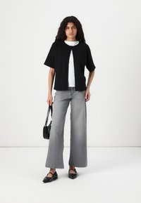Black short-sleeve cardigan over a white shirt, paired with wide-leg gray jeans and black flats, featuring decorative studs and a small handbag.
