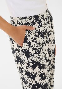 Pantalons à imprimé floral noir et blanc avec une taille élastique et des poches latérales, présentant une texture de tissu douce et une coupe ample.