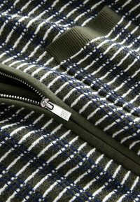 Tissu tricoté à rayures vertes et blanches avec des accents bleus, présentant une fermeture éclair argentée et un détail de poignet côtelé vert.
