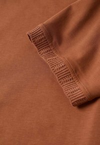 Haut marron à manches courtes avec un ourlet côtelé texturé. Tissu lisse présentant une couleur unie sans motifs ni ornements.