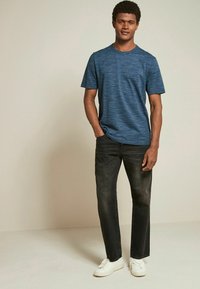Tricou scurt cu mânecă, texturat, de culoare albastră, asociat cu blugi închis la culoare și adidași albi. Croi lejer, design minimalist, material neted.