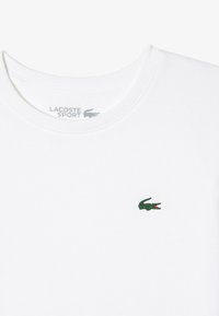 White cotton t-shirt featuring a green embroidered crocodile logo on the left chest and a round crew neckline.