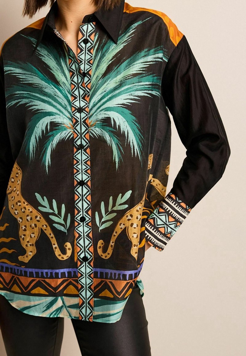 Chemise noire boutonnée avec un motif de palmier et d'imprimé léopard en turquoise et orange, avec des motifs géométriques sur les poignets et la patte de boutonnage.