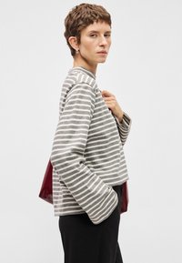 Sweatshirt cinza e creme com riscas, de corte cropped, mangasLongas e decote redondo, combinado com calças pretas e uma bolsa bordô.