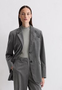 Gray corduroy blazer with a notched collar, two buttons, and a chest pocket, paired with a textured gray turtleneck sweater and matching pants.