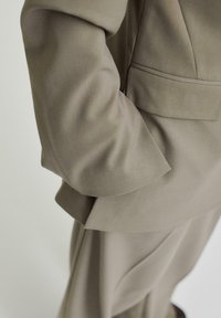 Beige kavaj med skräddarsydd passform, mjuk textur och en sidficka, med vikta ärmar och rena linjer.