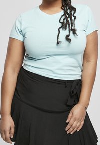 Světle modré tričko s výstřihem do V vyrobené z měkké látky, spárované s černou sukní s páskem v pase a vrstveným lemem.