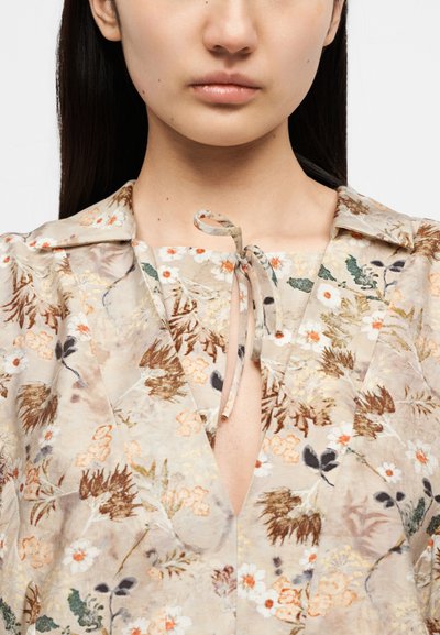 Μπλούζα με φλοράλ σχέδιο σε ανοιχτό μπεζ χρώμα, με λαιμόκοψη διαχωρισμένη, γιακά και κλείσιμο με κορδόνι. Κατασκευασμένη από λείο, ελαφρύ ύφασμα.