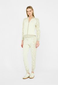 Tuta a due pezzi color crema, con dettagli a stampa leopardata sulle maniche e sui pantaloni. Realizzato in tessuto morbido con polsini e orlo a coste.