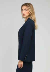 Blazer marine en tissu lisse, au look ajusté, avec des revers en pointe et des boutons dorés sur les manches.